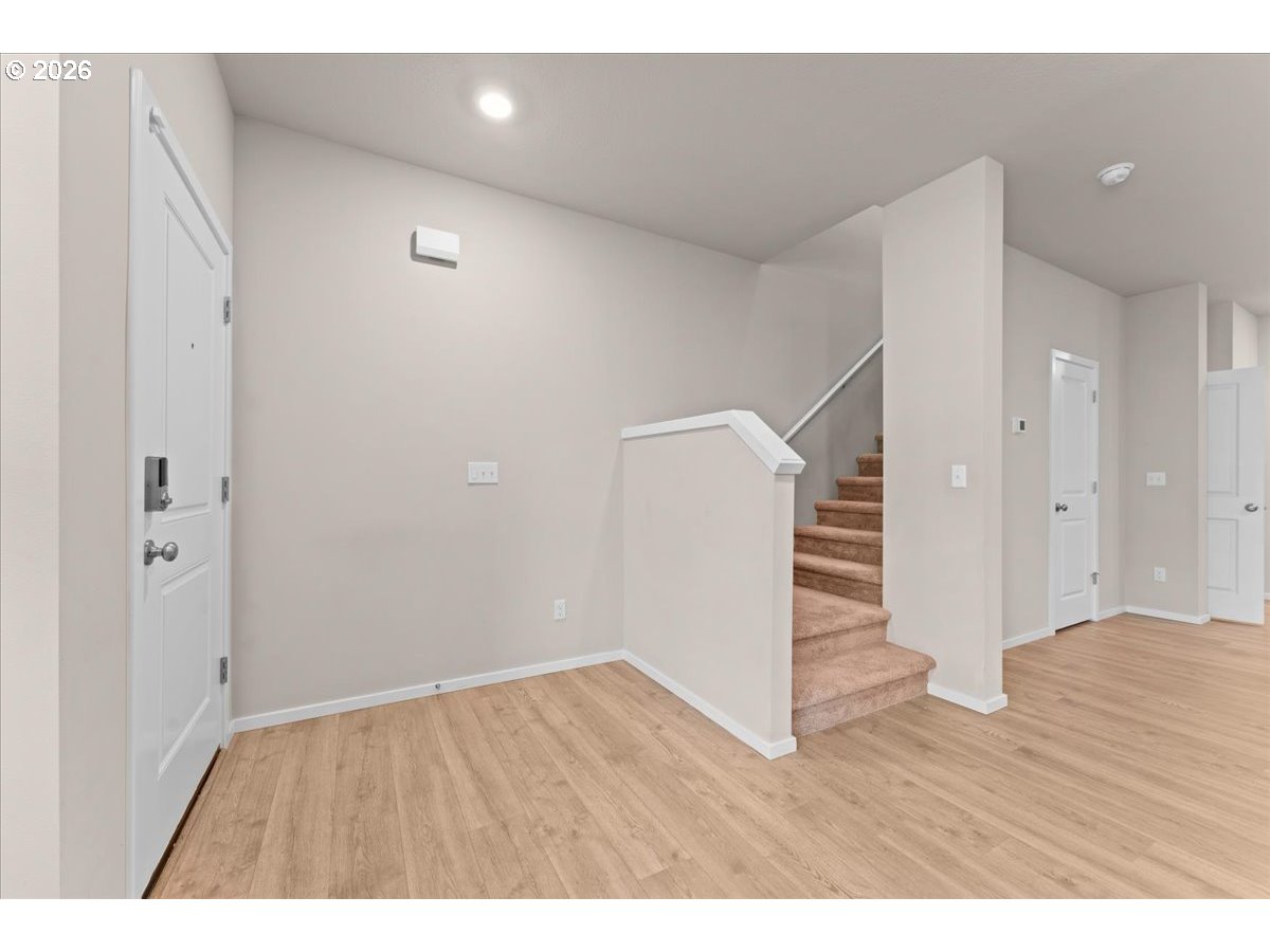 Entry hall with light wood floors, a white front door, and carpeted stairs.