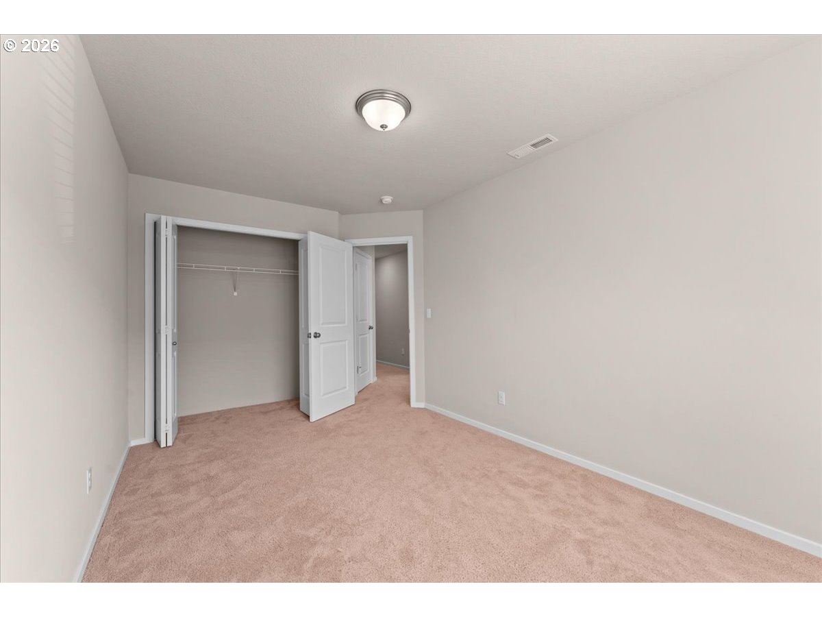 Empty bedroom with beige carpet, an open closet, and a doorway to the adjoining room.