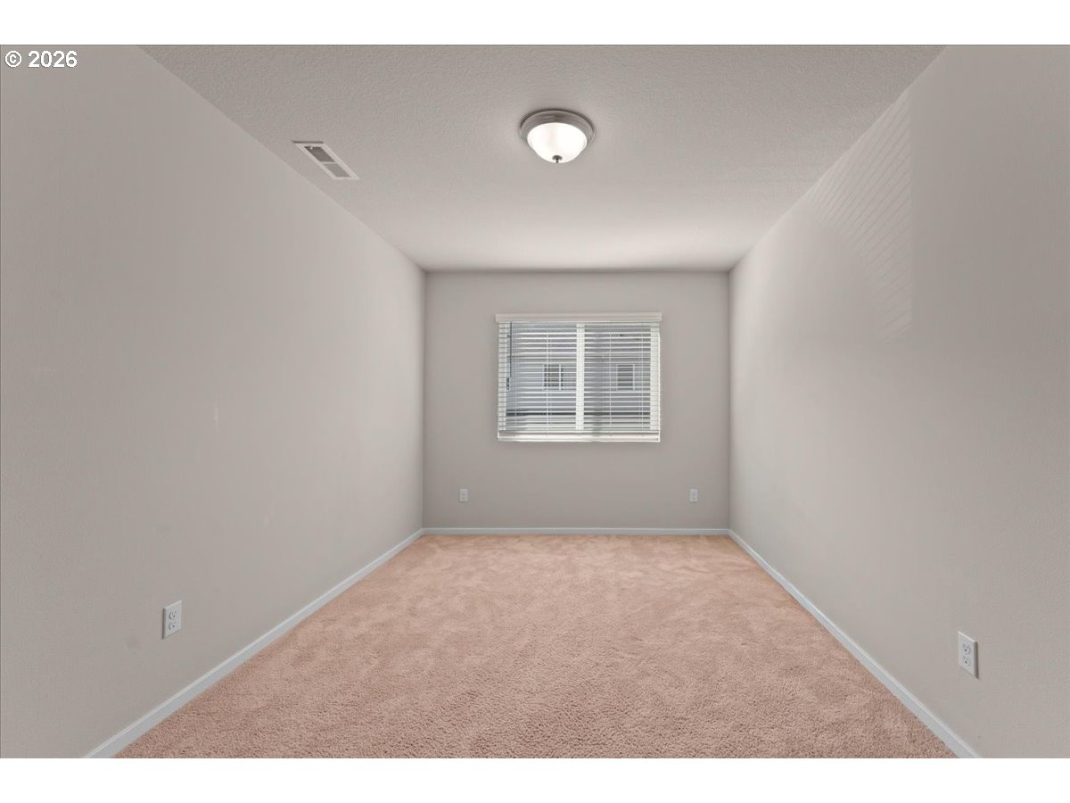 Empty bedroom with beige carpet and a window fitted with horizontal blinds.