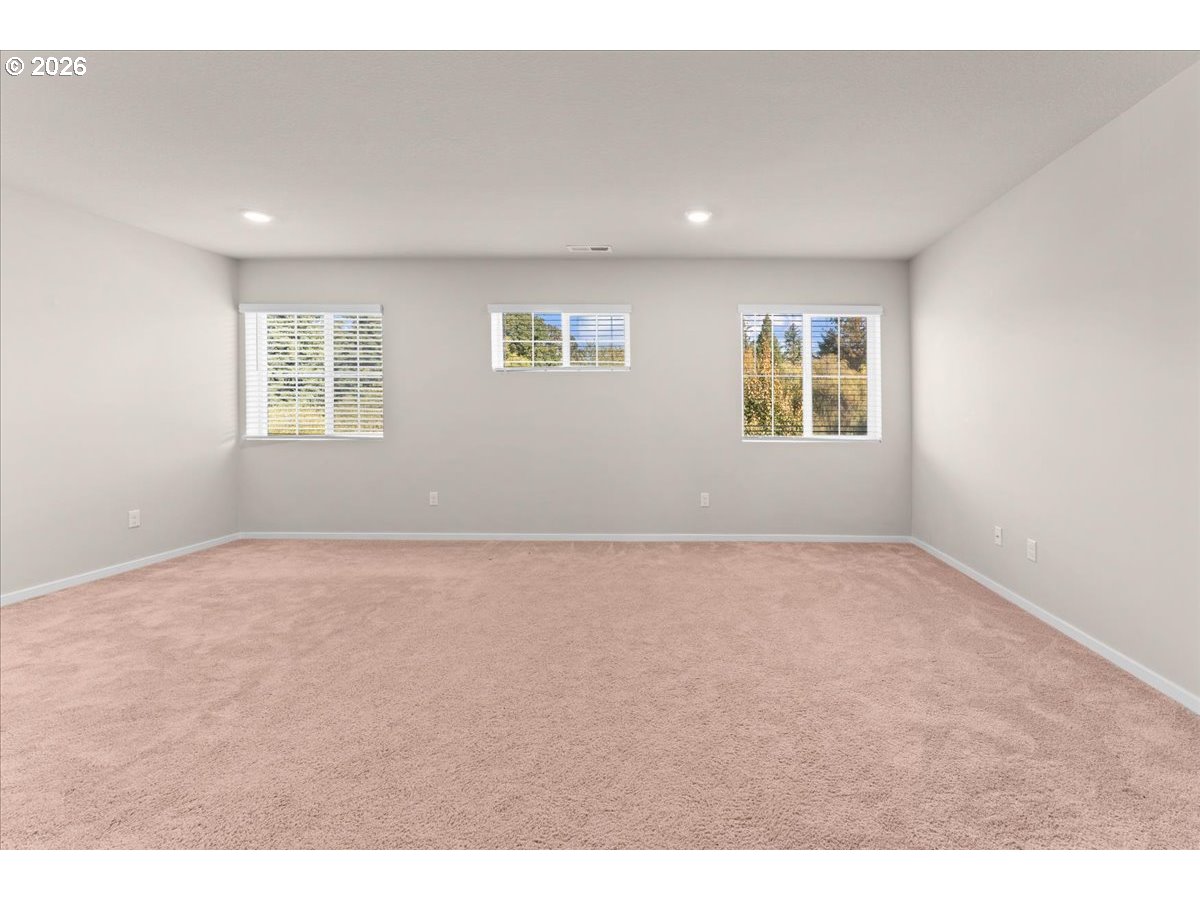 Empty carpeted room with light gray walls and three windows with white blinds.