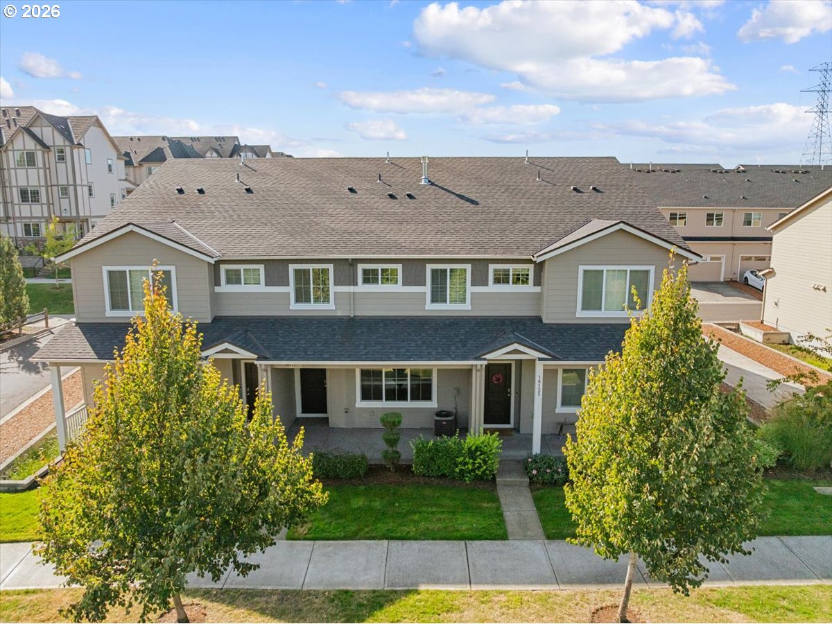 Two-story gray townhouse with a covered entry, front lawn, and leafy trees.