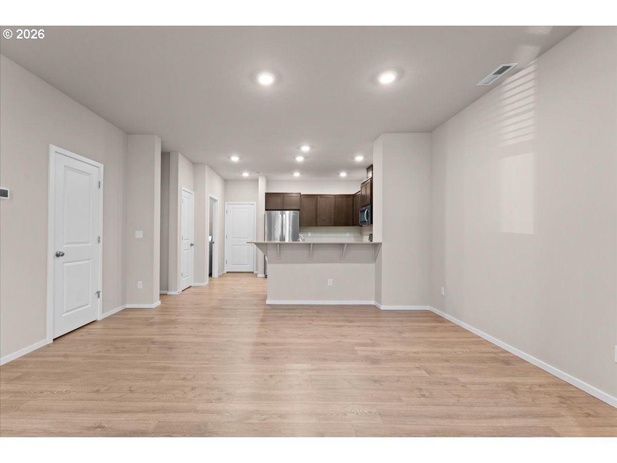 Empty open-plan living area with light wood-look floors and a kitchen with dark cabinets and stainless steel appliances.