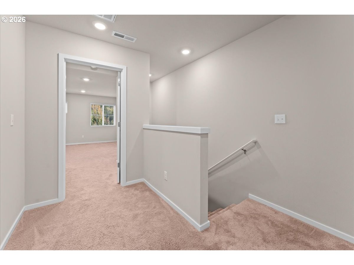 Carpeted upstairs landing with stairs and an open doorway to a room with a window.
