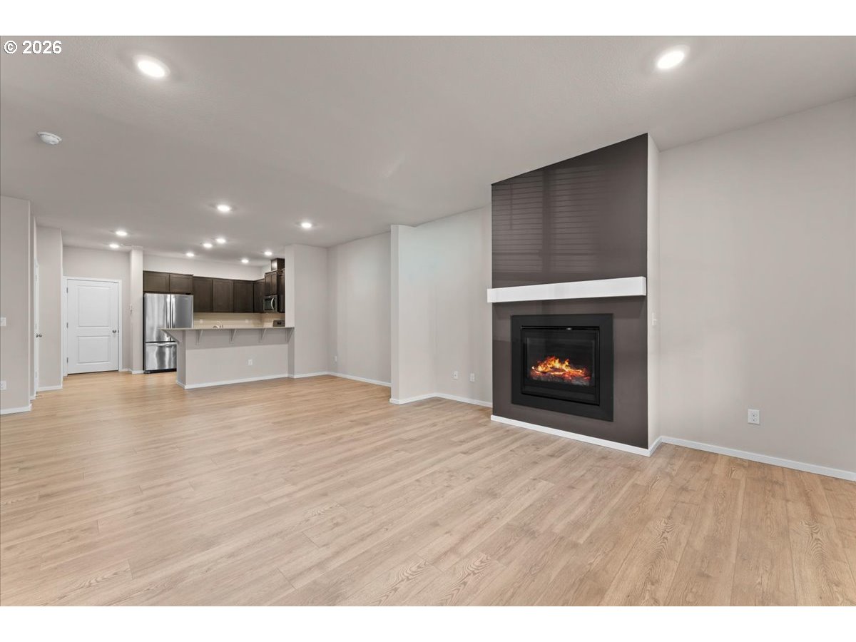 Open-plan living room with light wood floors, a modern fireplace, and adjoining kitchen.