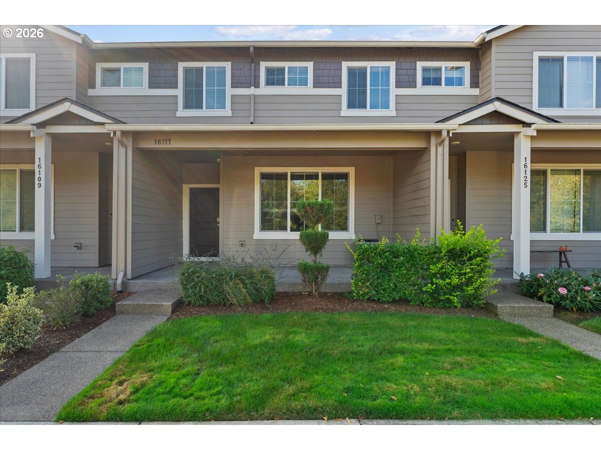 Gray two-story attached home with a covered entry, front lawn, and shrubs.