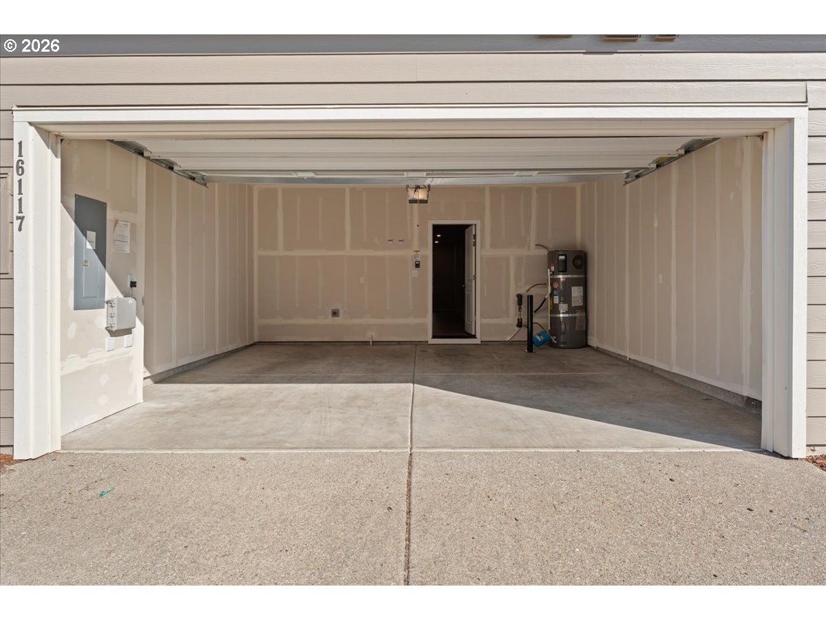 Open, empty garage with unfinished drywall, a concrete floor, and a water heater.