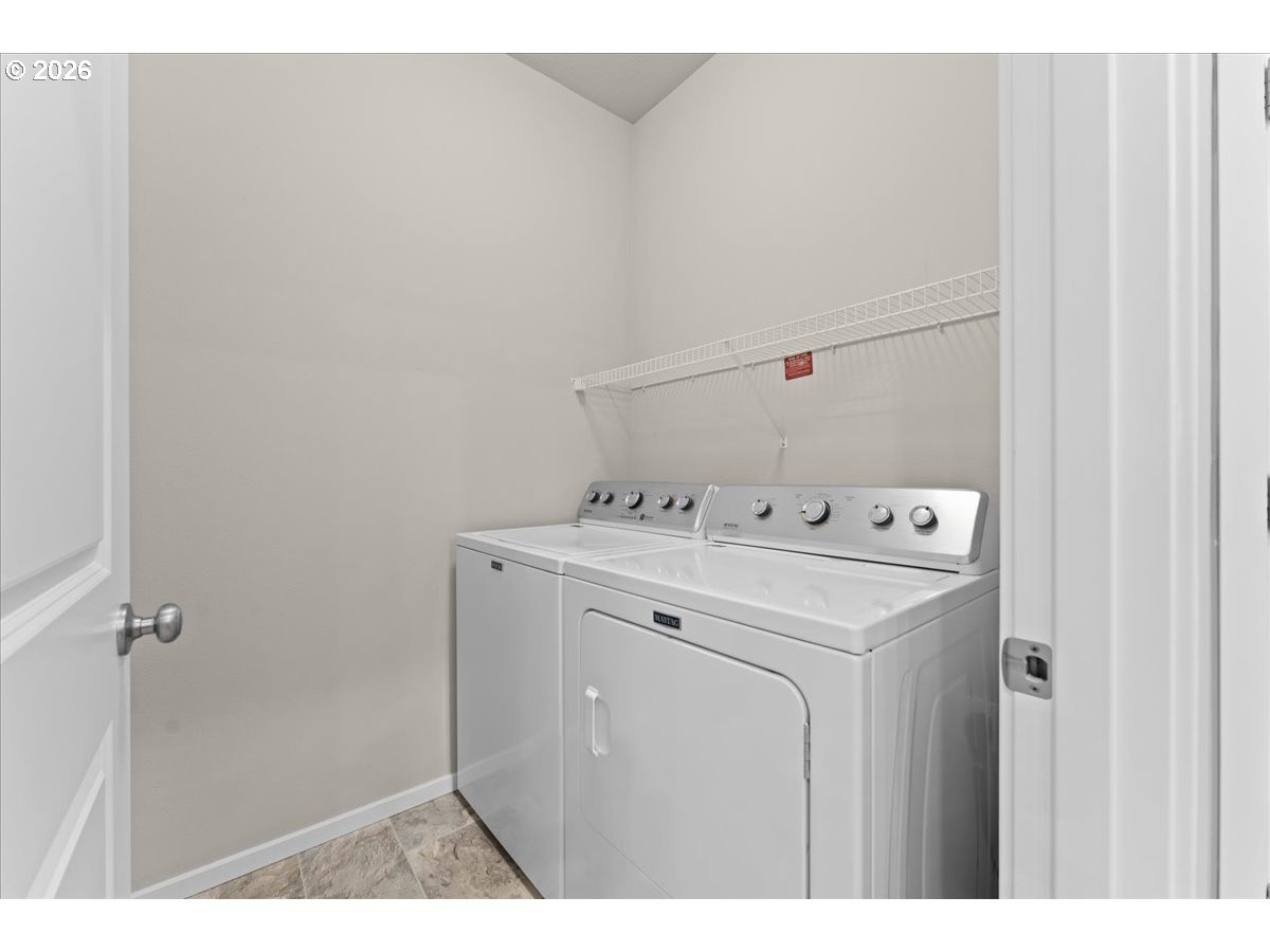 Laundry room with a white washer and dryer beneath a wire shelf.