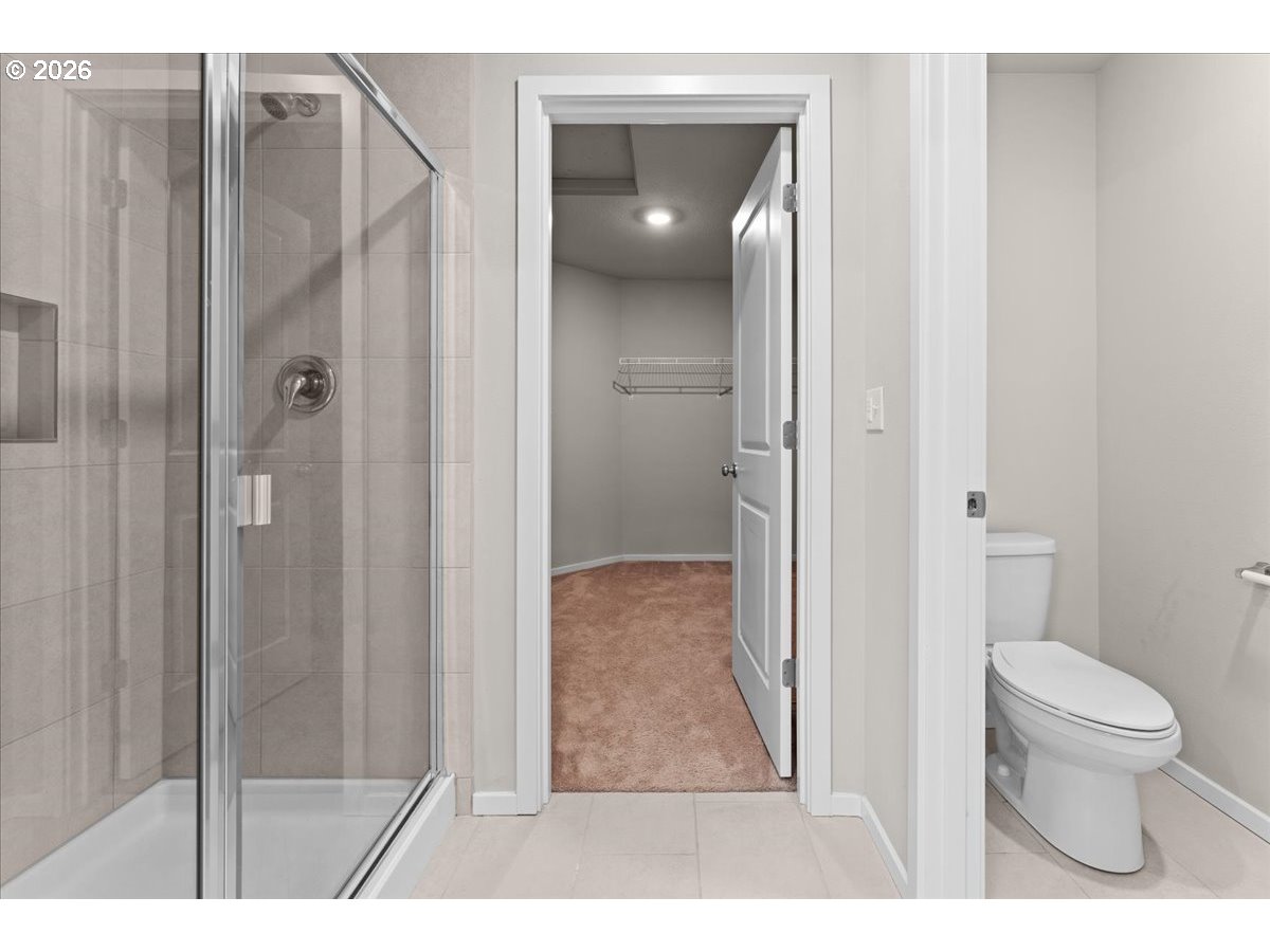 Bathroom with a glass-enclosed tiled shower, toilet, and doorway to an empty carpeted closet.