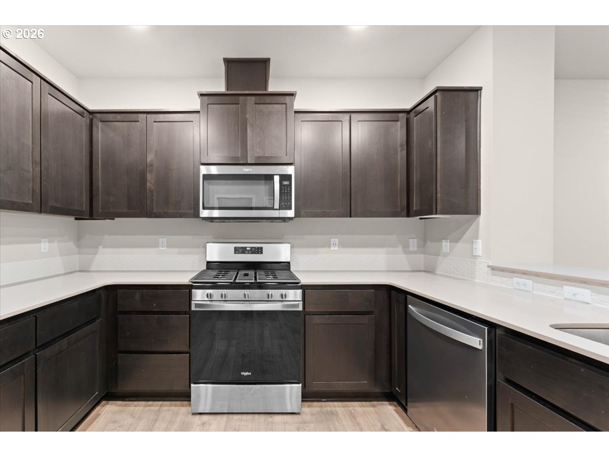 Kitchen with dark cabinetry, white countertops, and stainless steel gas range and microwave.