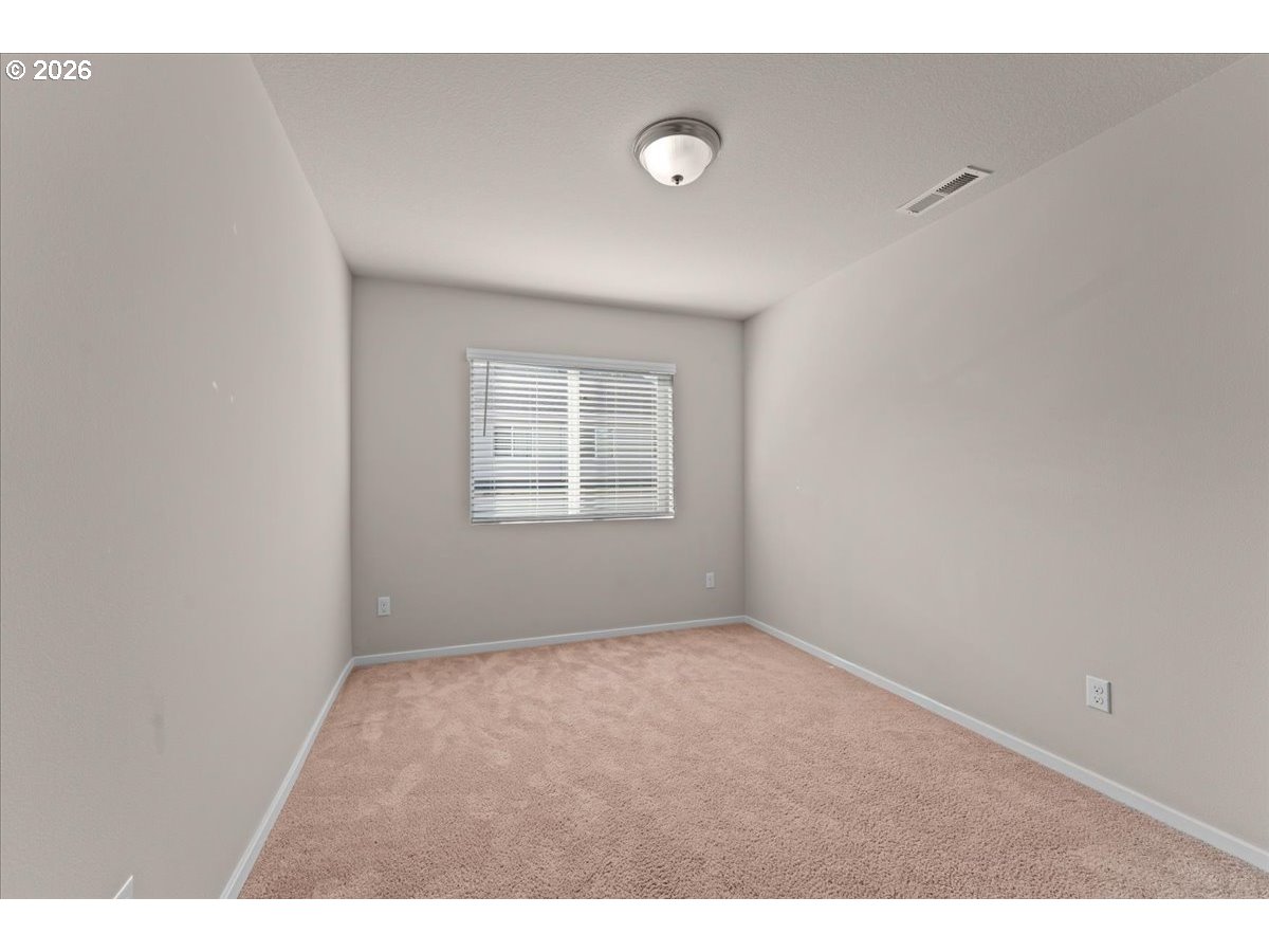 Empty bedroom with beige carpet and a window with white blinds.