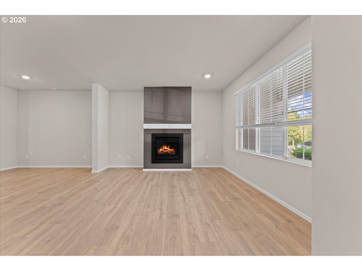 Empty living room with light wood flooring, a fireplace, and large windows with blinds.
