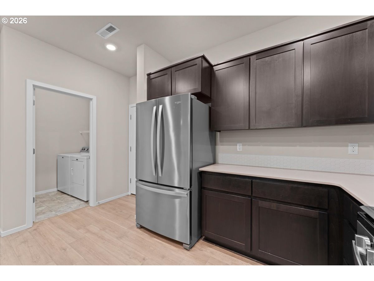 Kitchen with dark cabinetry, a stainless steel refrigerator, and a laundry area through the doorway.