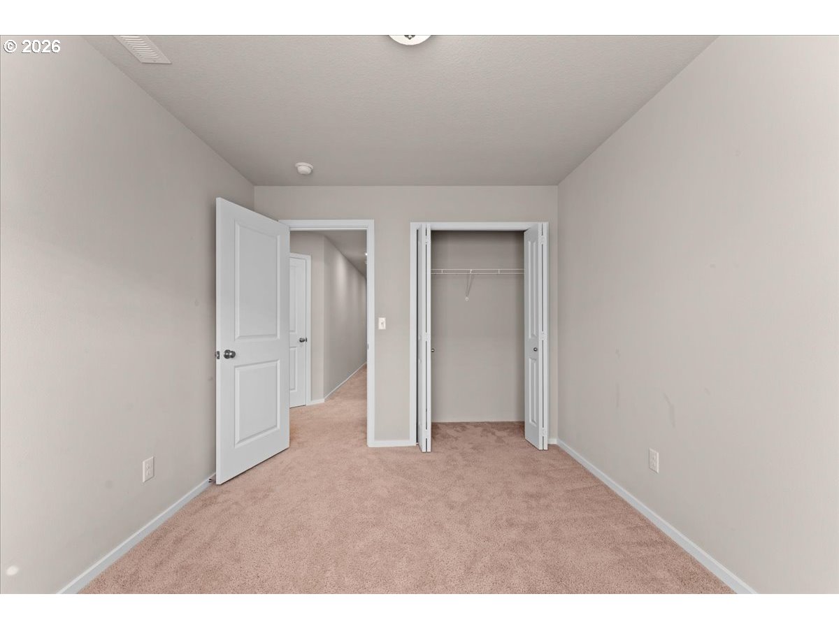 Empty carpeted room with an open closet and doorway to the hallway.