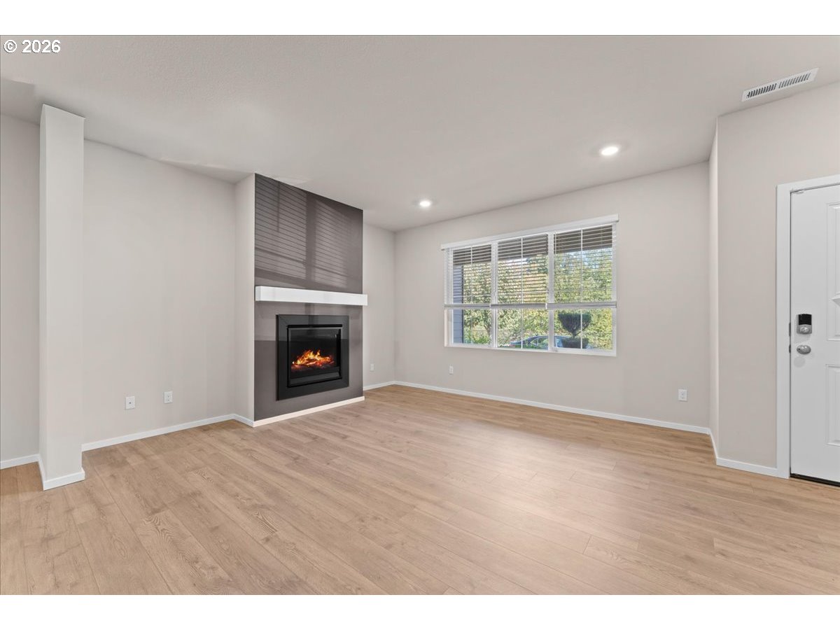 Vacant living room with light wood floors, a modern fireplace, and a large window with blinds.
