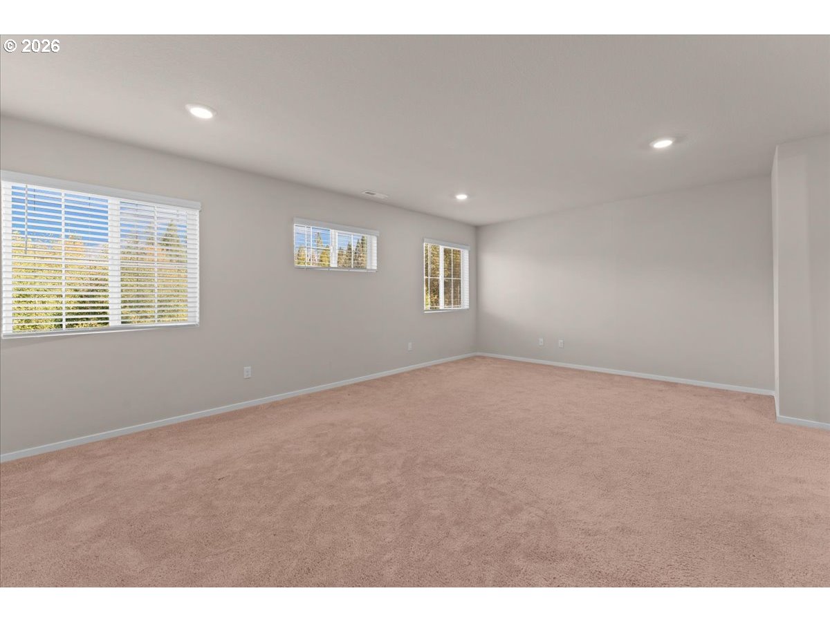 Empty carpeted room with three windows, white blinds, and recessed ceiling lights.
