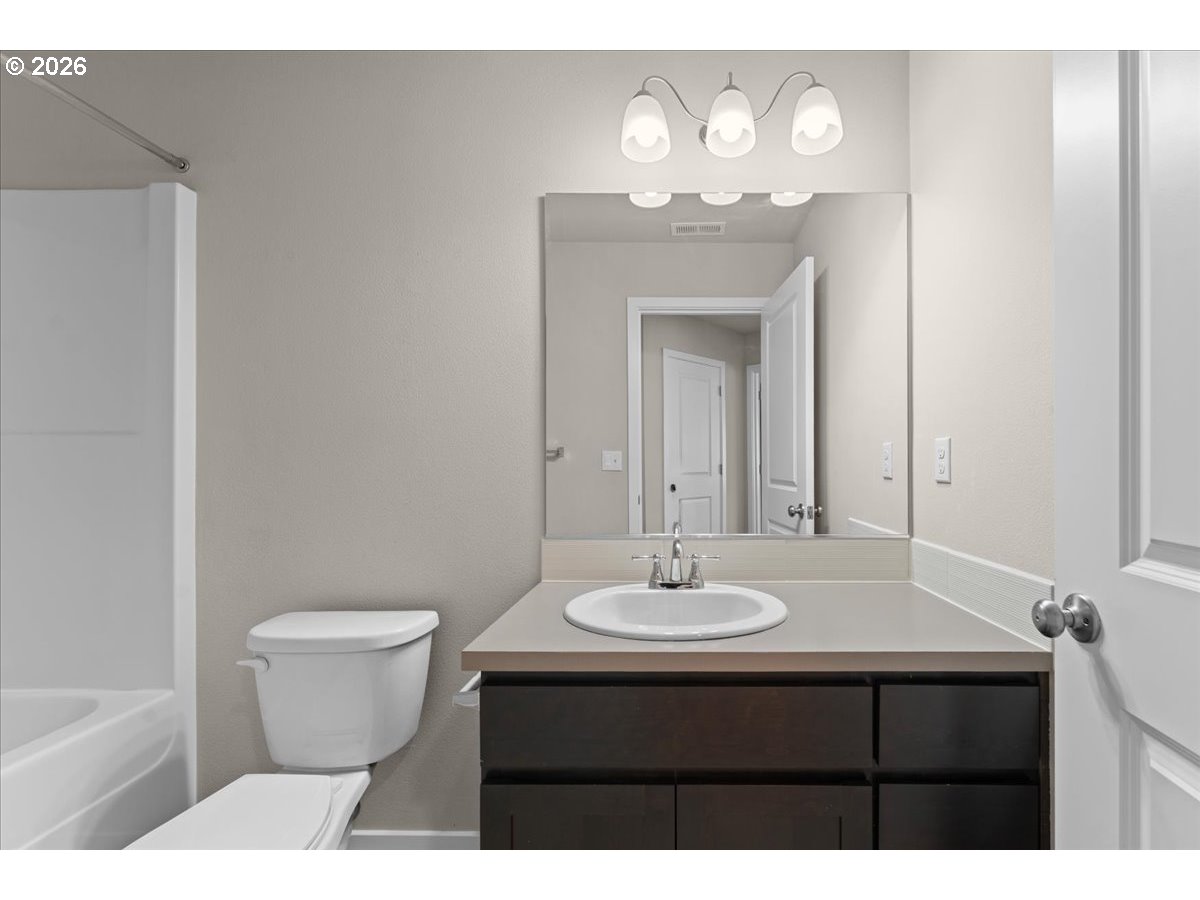 Bathroom with a dark wood vanity, large mirror, toilet, and bathtub.