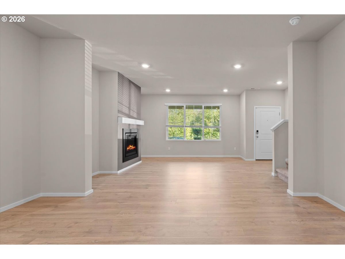 Vacant living room with light wood flooring, a modern fireplace, and a large window.