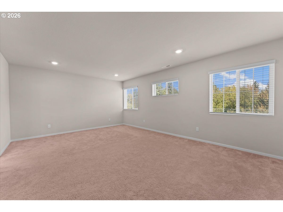 Empty carpeted room with three windows fitted with white blinds.