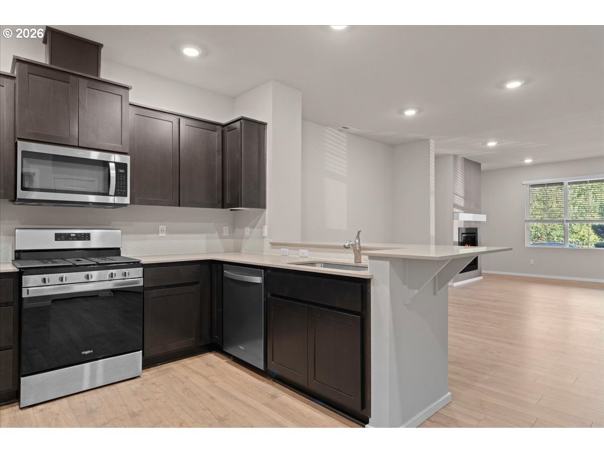 Kitchen with dark cabinets, stainless steel appliances, and a breakfast bar opening to a bright living area.