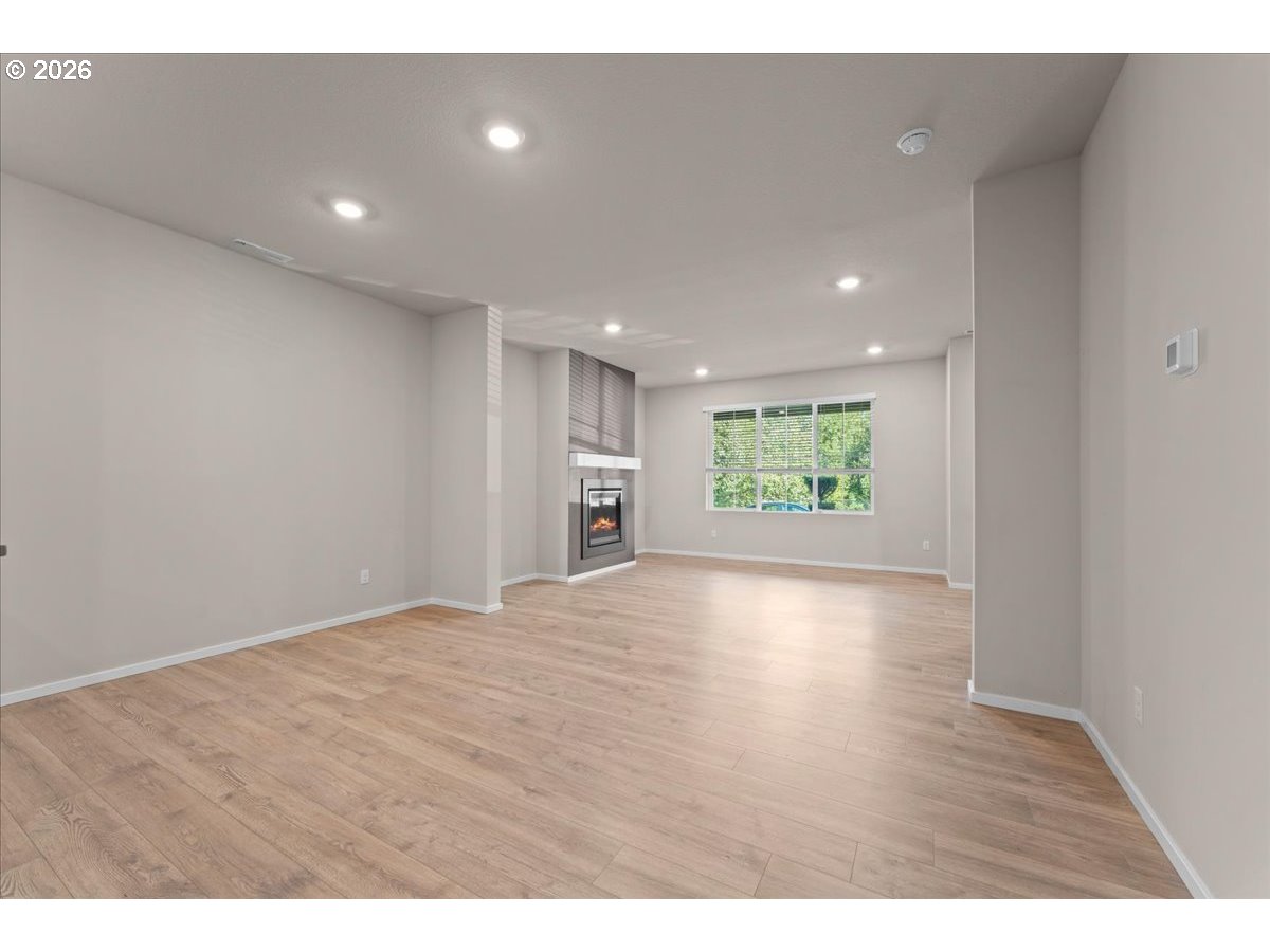 Vacant living room with wood-look floors, a built-in fireplace, and a large window with blinds.
