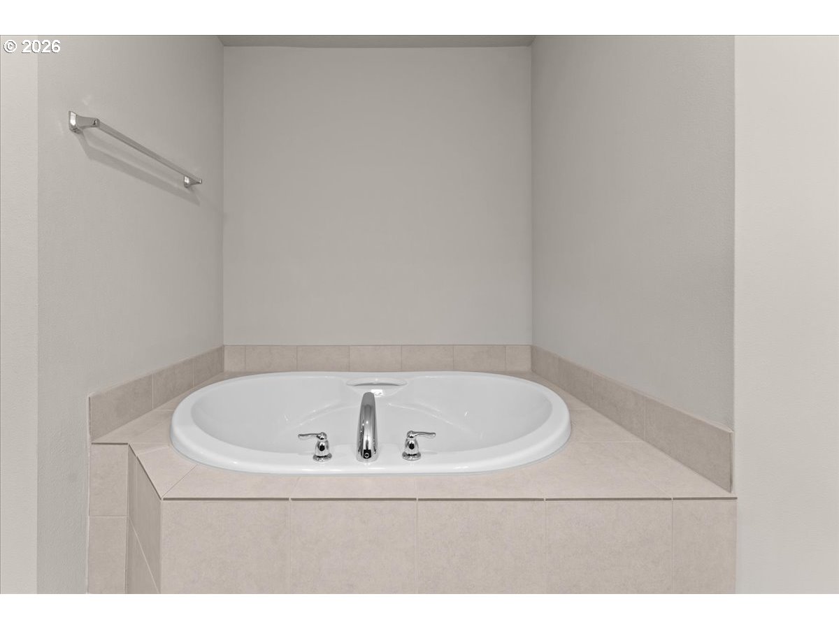 Oval white bathtub with beige tiled surround and chrome fixtures.