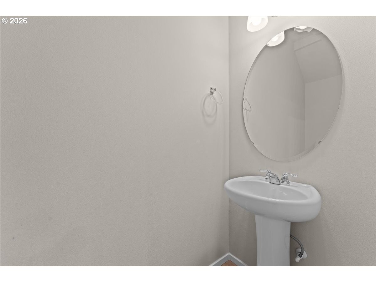 Bathroom pedestal sink with an oval mirror and chrome towel ring.