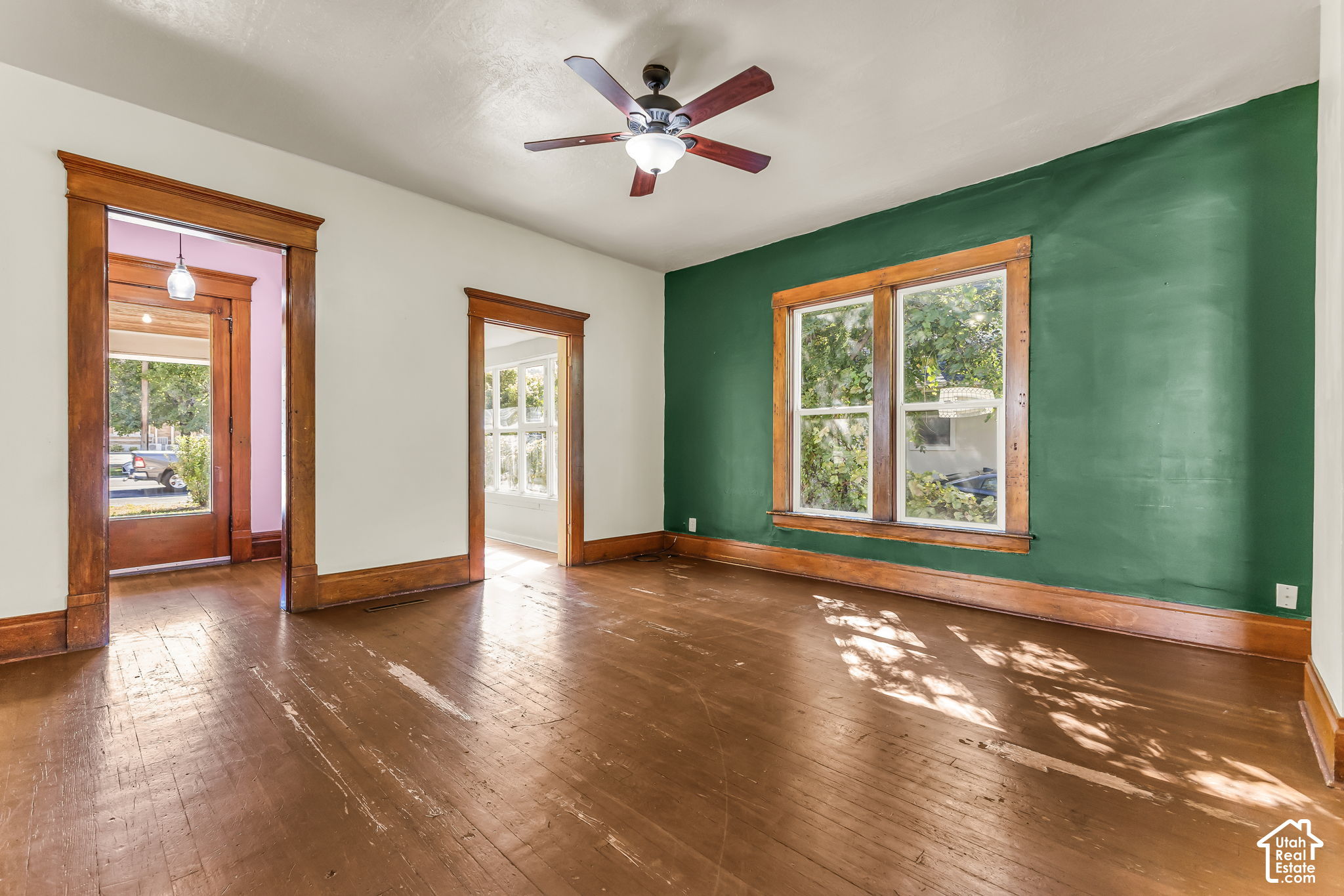 Empty room with hardwood floors, dark wood trim, a green accent wall, and a ceiling fan.