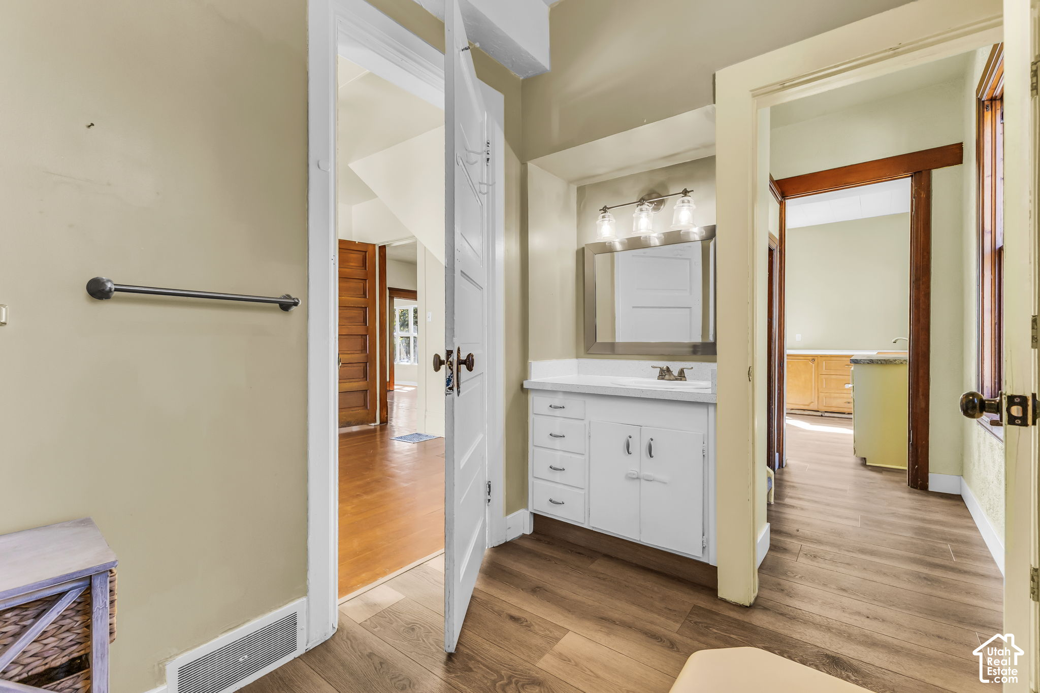 Bathroom vanity with a white sink cabinet and mirror, opening onto wood-floored adjoining rooms.