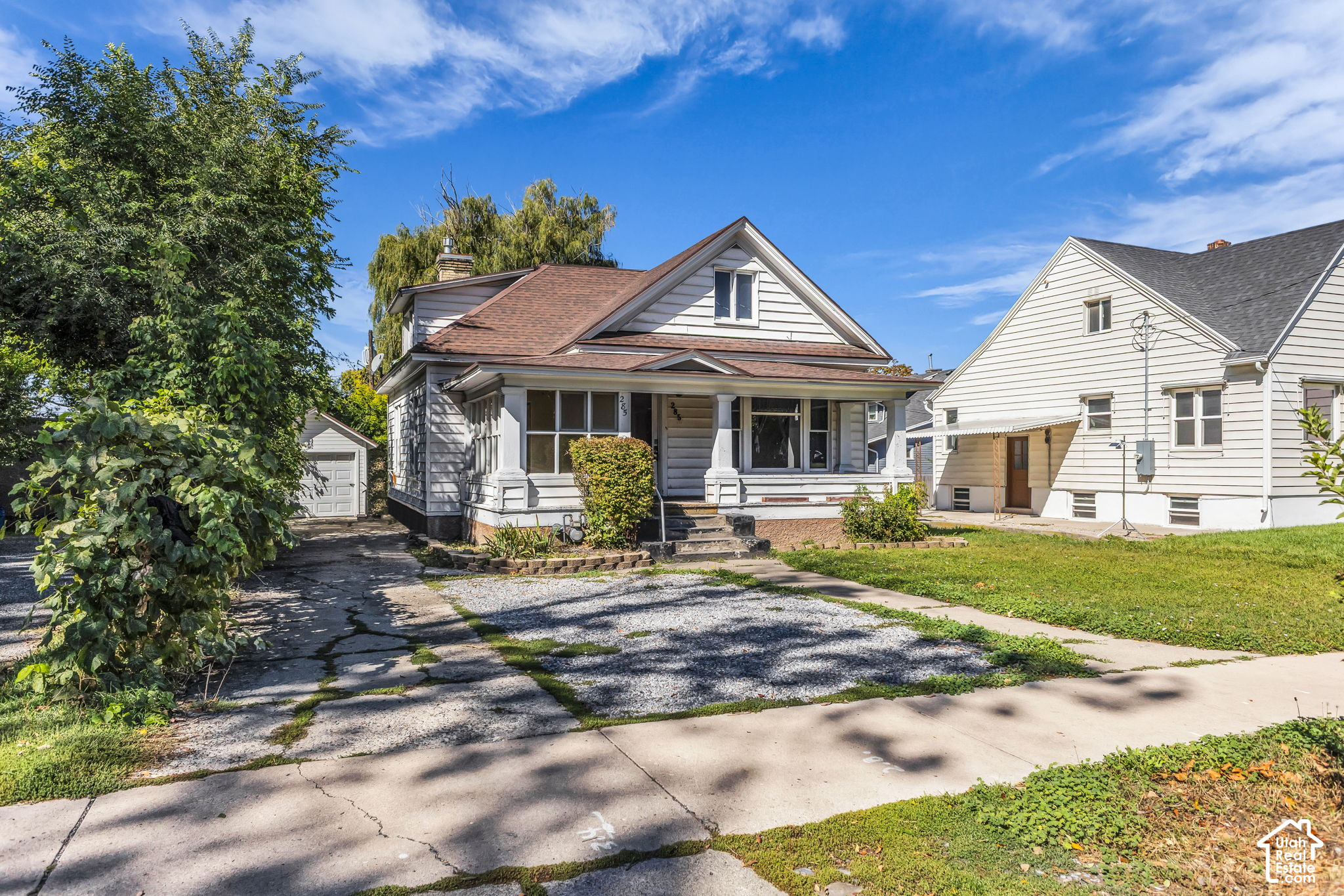 Gray-sided house with a covered front porch, steep gabled roof, and gravel driveway.