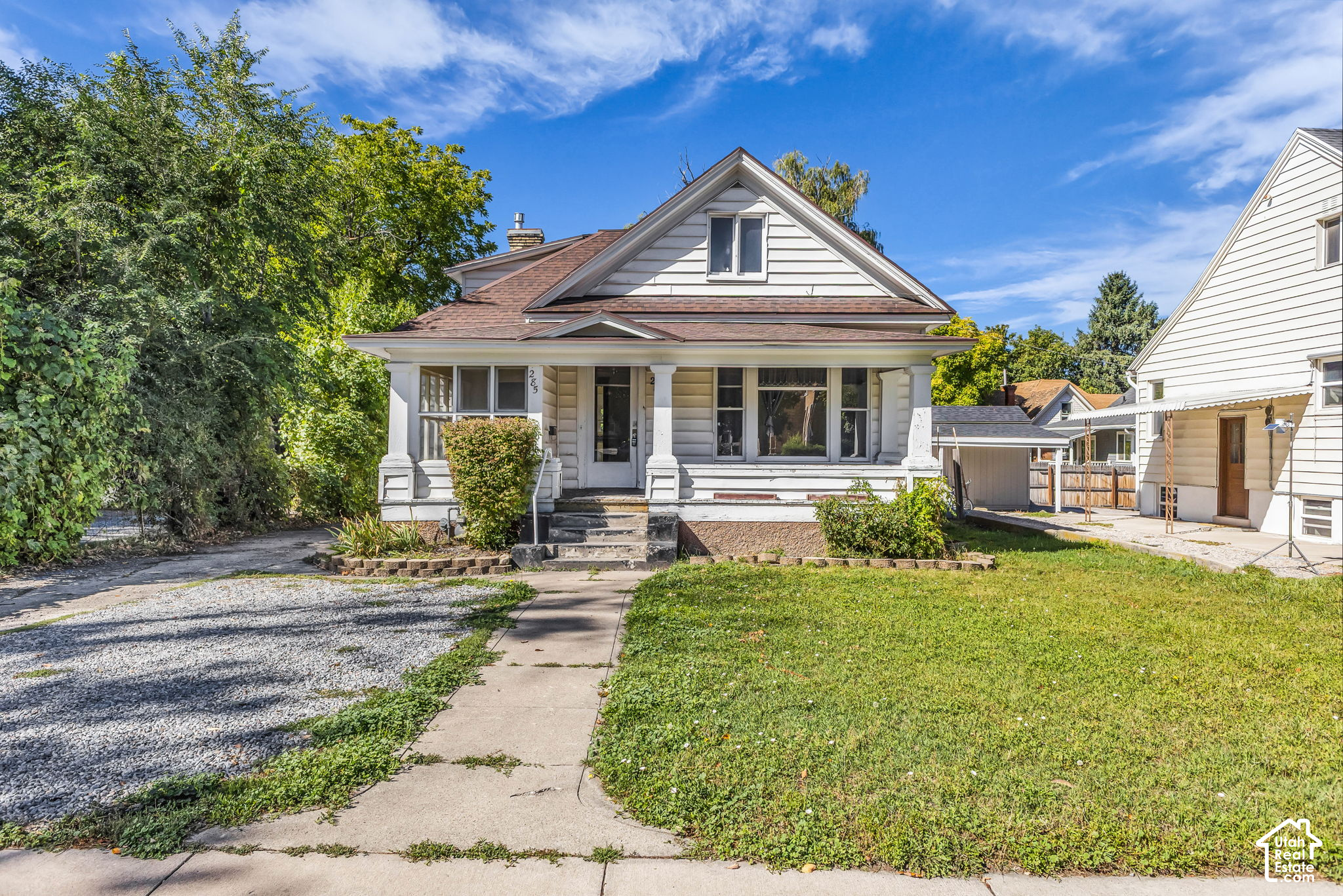 White-sided house with a covered front porch, prominent gabled roof, and gravel driveway.