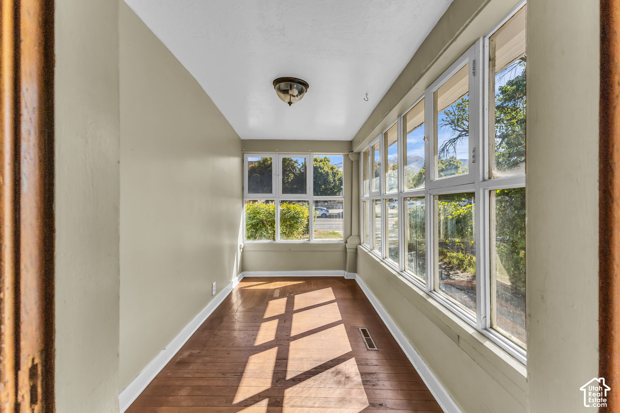 Empty sunroom with broad windows and sunlight casting geometric shadows across its wood floor.