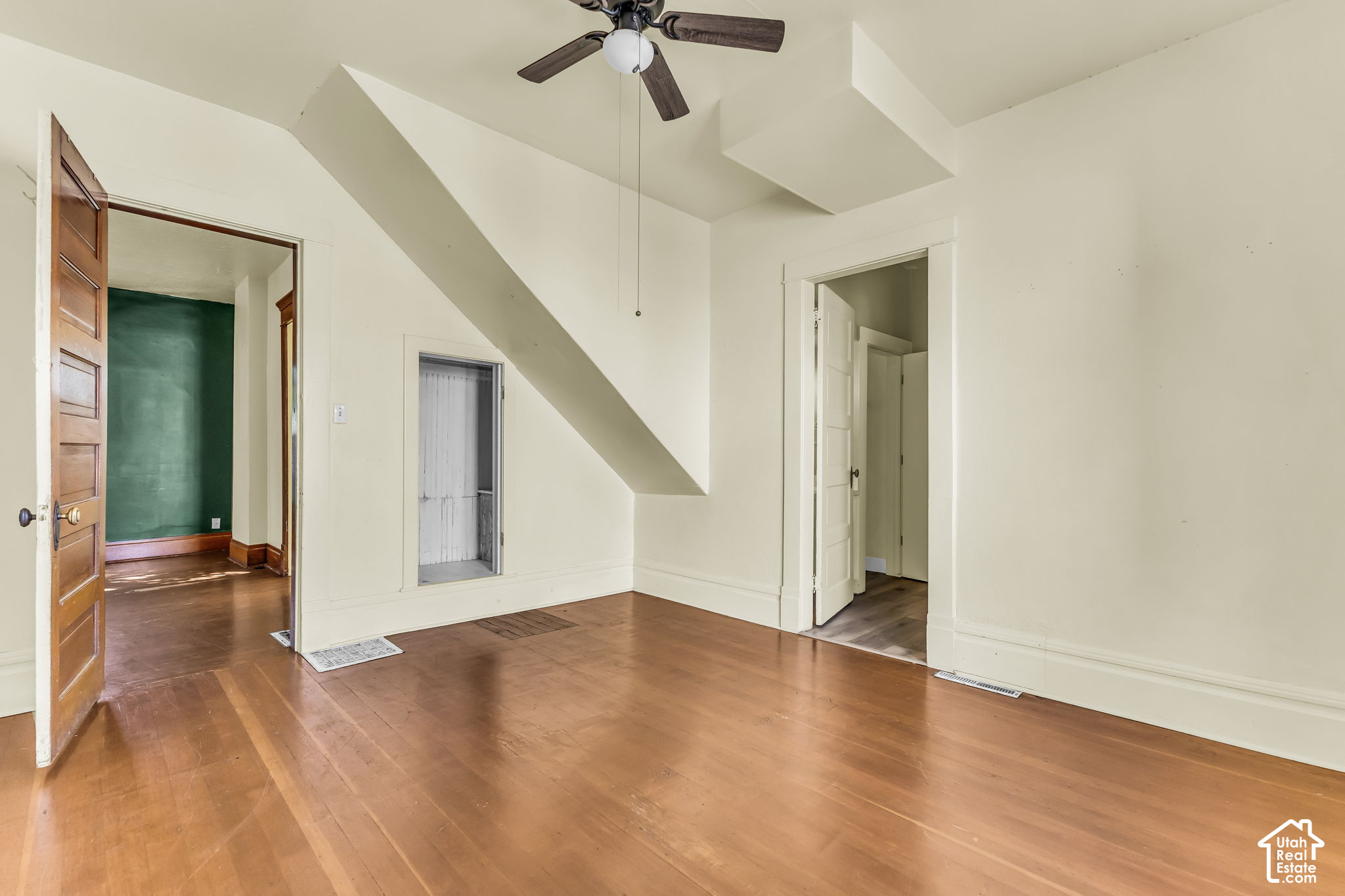 Vacant room with polished wood floors, a ceiling fan, and a doorway opening to a green-walled room.