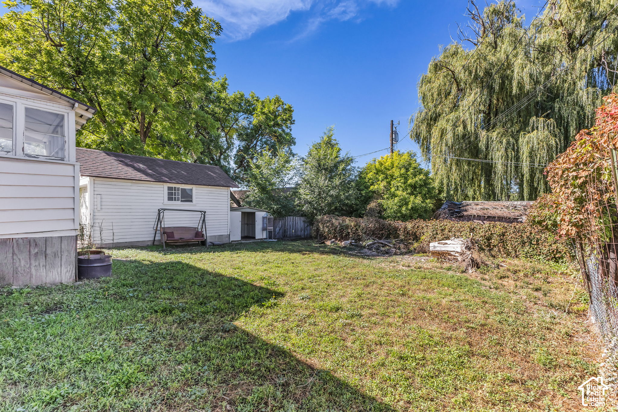 Backyard with a lawn, garden swing, small outbuildings, and mature trees.