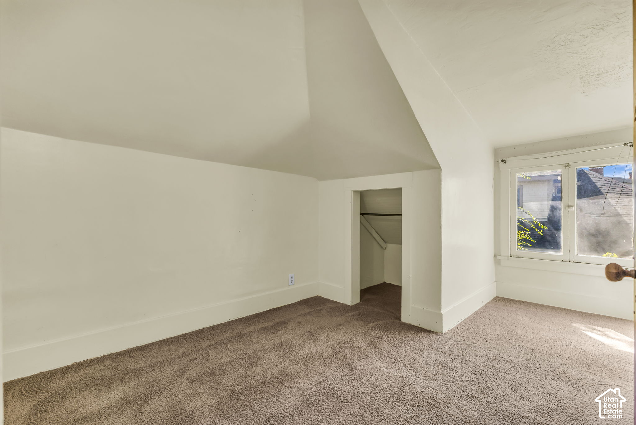 Vacant carpeted room with a sharply sloped ceiling and a sunlit window.