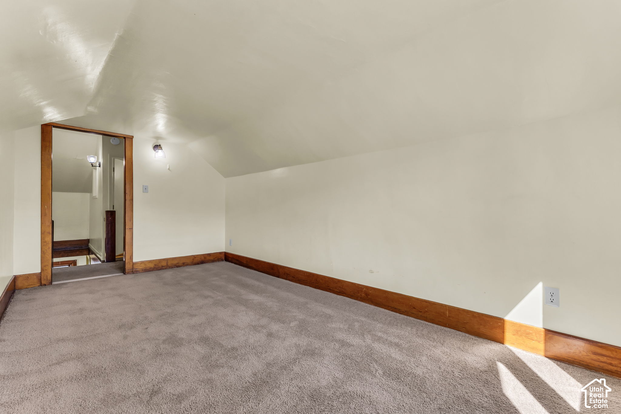 Empty carpeted room with a sloped ceiling, wood trim, and a large mirror by the doorway.