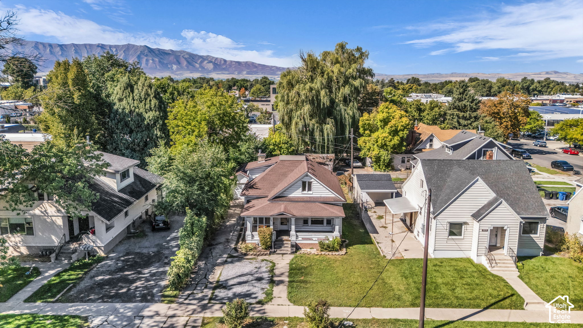 Aerial view of a white house with a brown roof, leafy neighborhood, and mountain range beyond.
