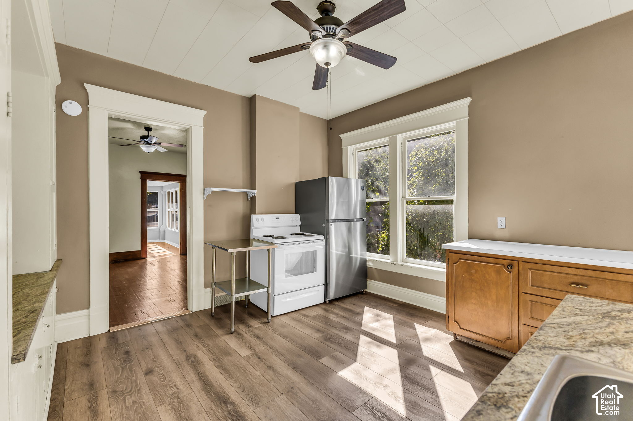 Vacant kitchen with stainless refrigerator, white range, large windows, and wood-look flooring.