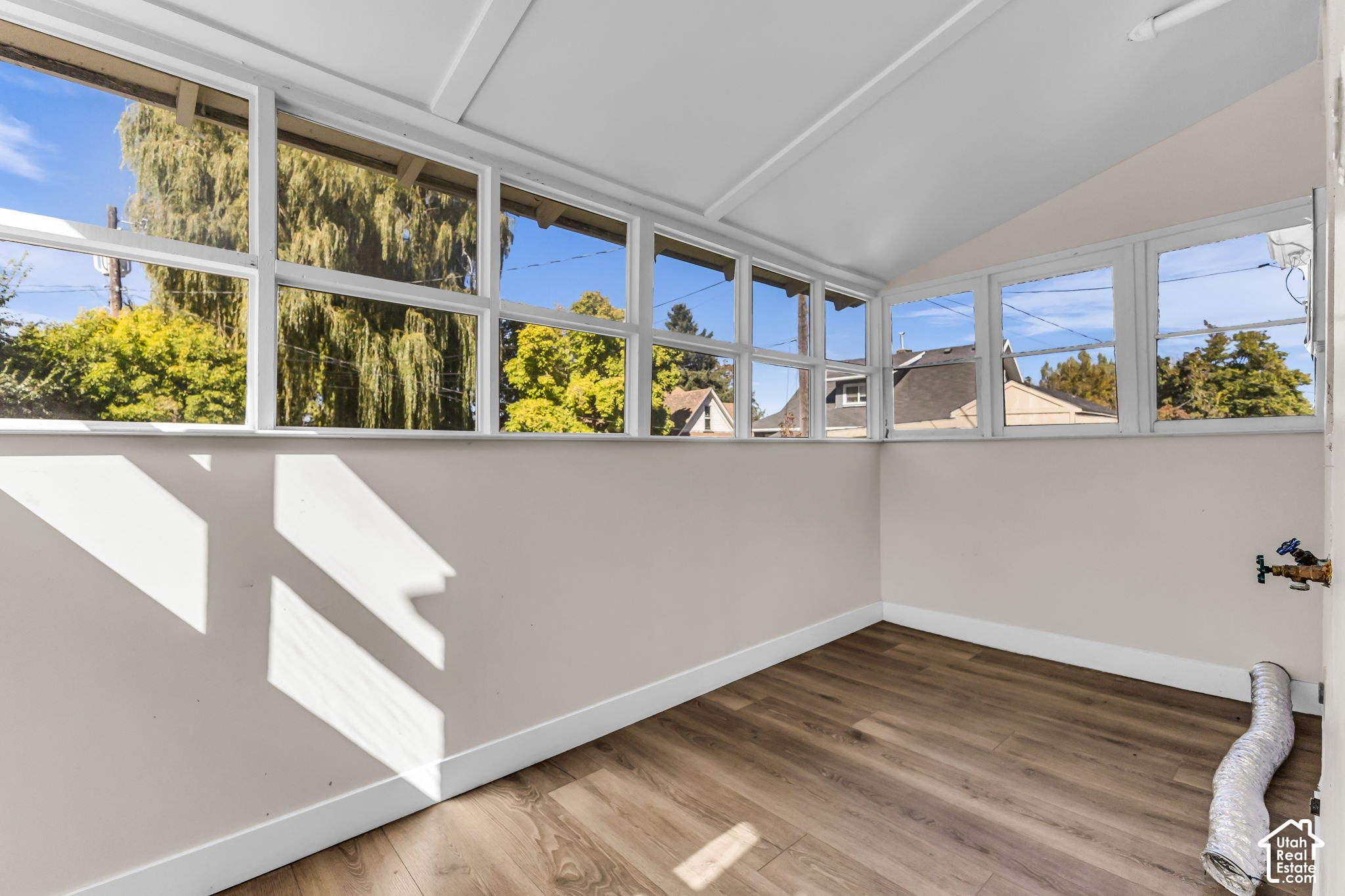 Bright empty room with wraparound windows and wood-look flooring.
