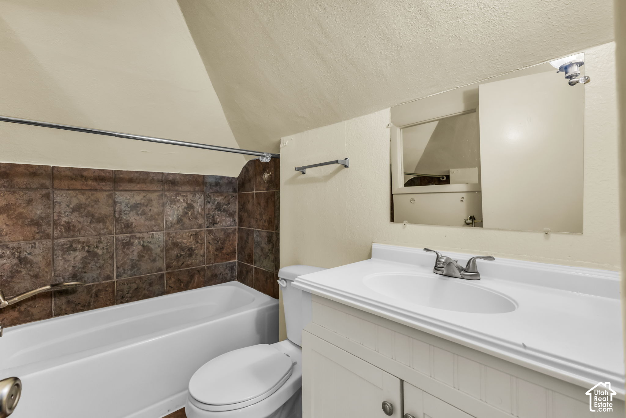Bathroom with a white bathtub, brown tiled surround, toilet, and vanity beneath a mirrored cabinet.