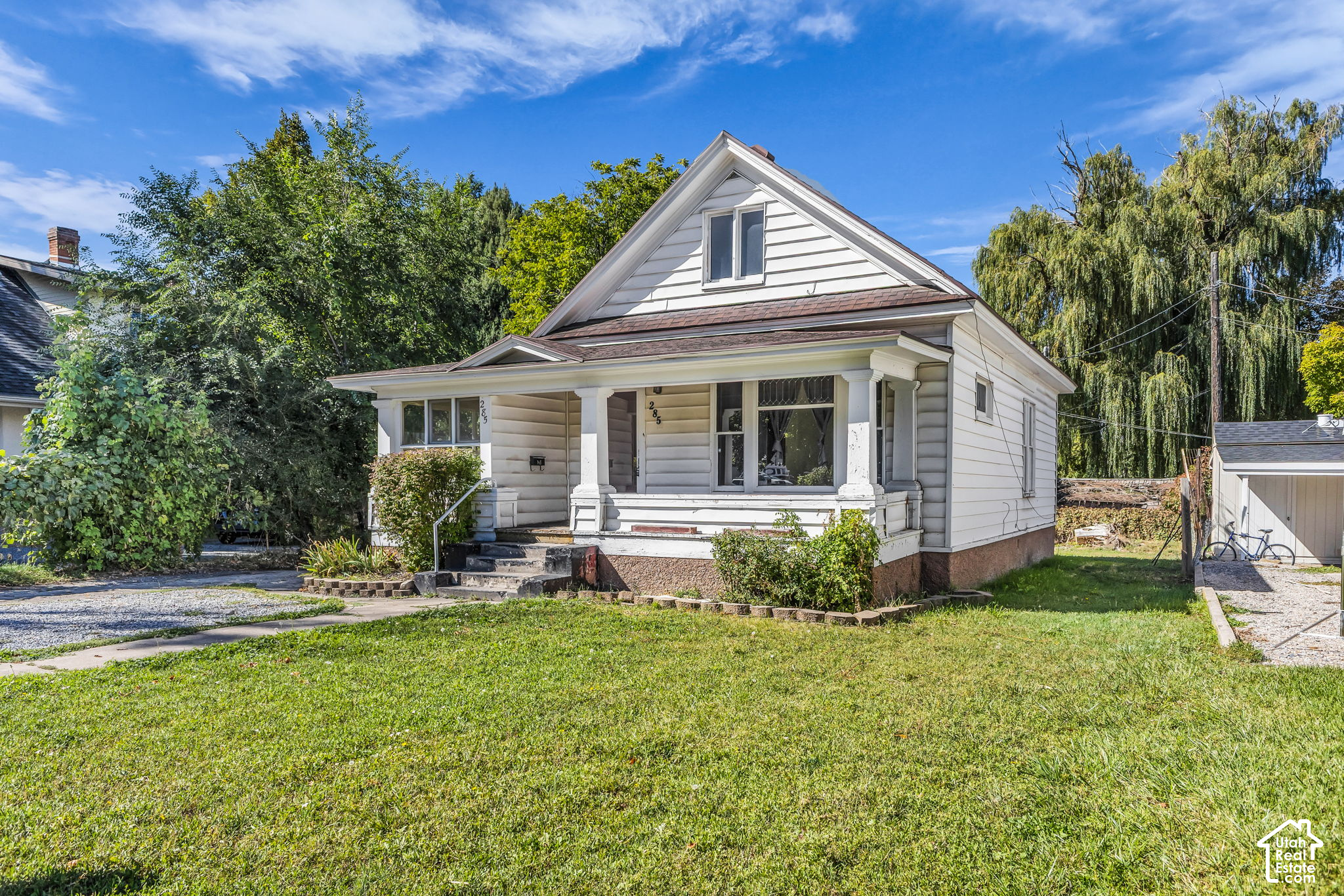 White gabled house with a covered porch, front steps, and a broad green lawn.