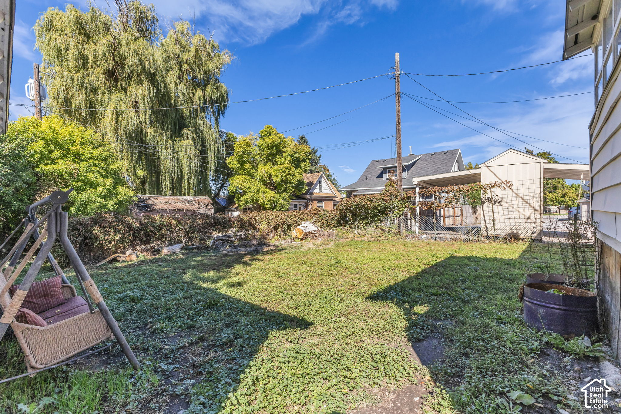 Backyard with a wicker swing, grassy lawn, raised garden beds, and mature trees.