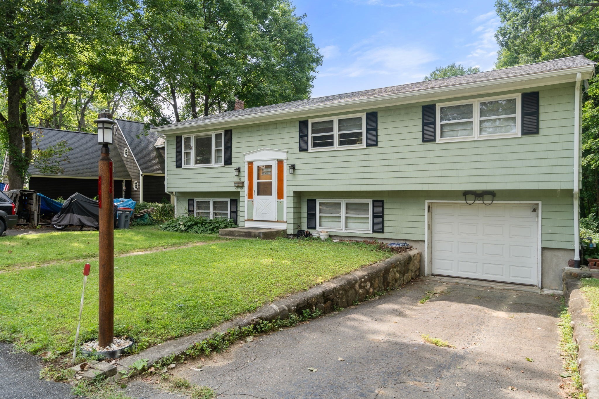 Green split-level home with dark shutters, a white garage door, and a tree-lined lawn.