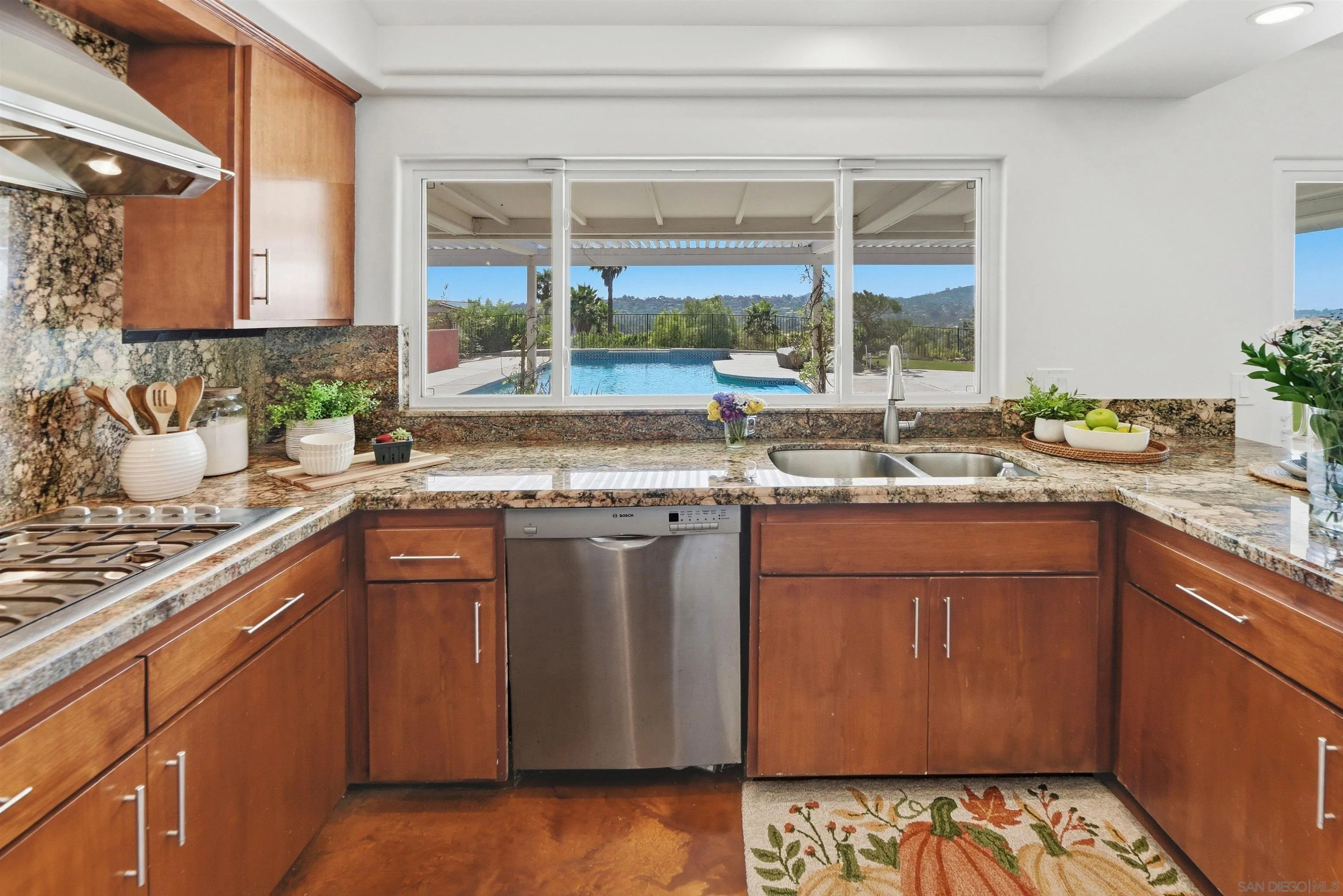 Kitchen with wood cabinetry and granite counters overlooking a backyard pool and rolling hills.