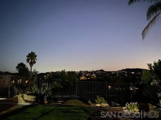 Dusk view of hillside homes and city lights from a landscaped backyard patio.