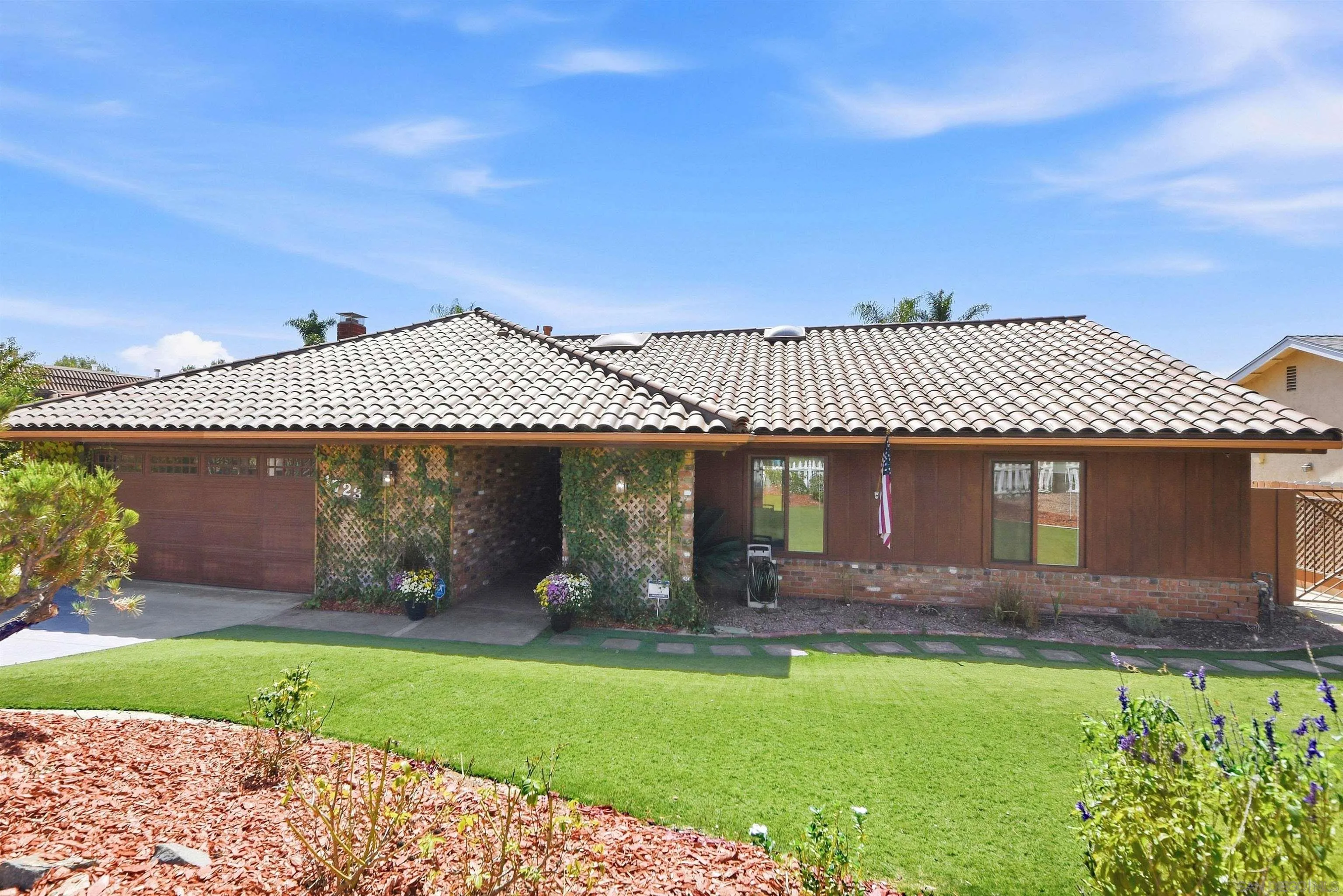 Single-story home with a tile roof, brown garage door, trellised entry, and landscaped front lawn.