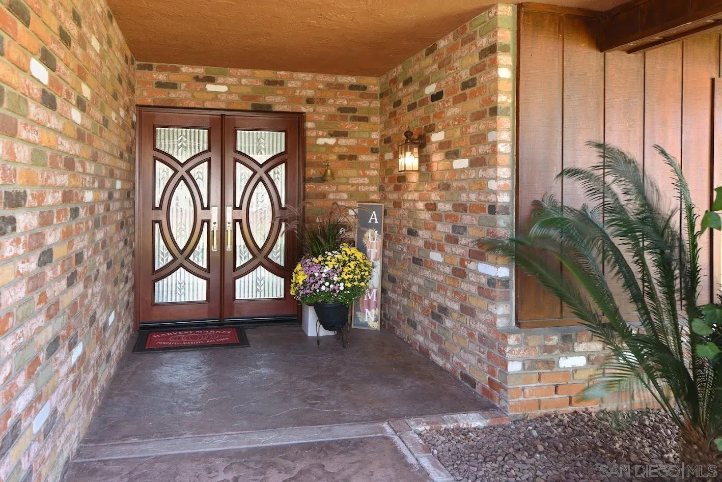 Brick-front entry with ornate double doors, a flower pot, and a covered stone porch.