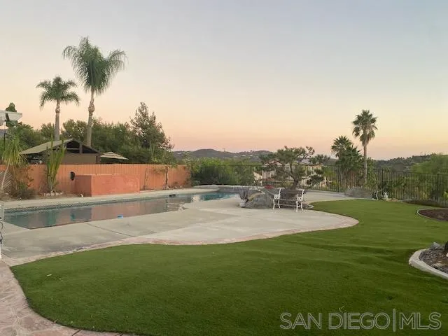 Backyard pool and lawn with palm trees, patio dining set, and distant hills at sunset.