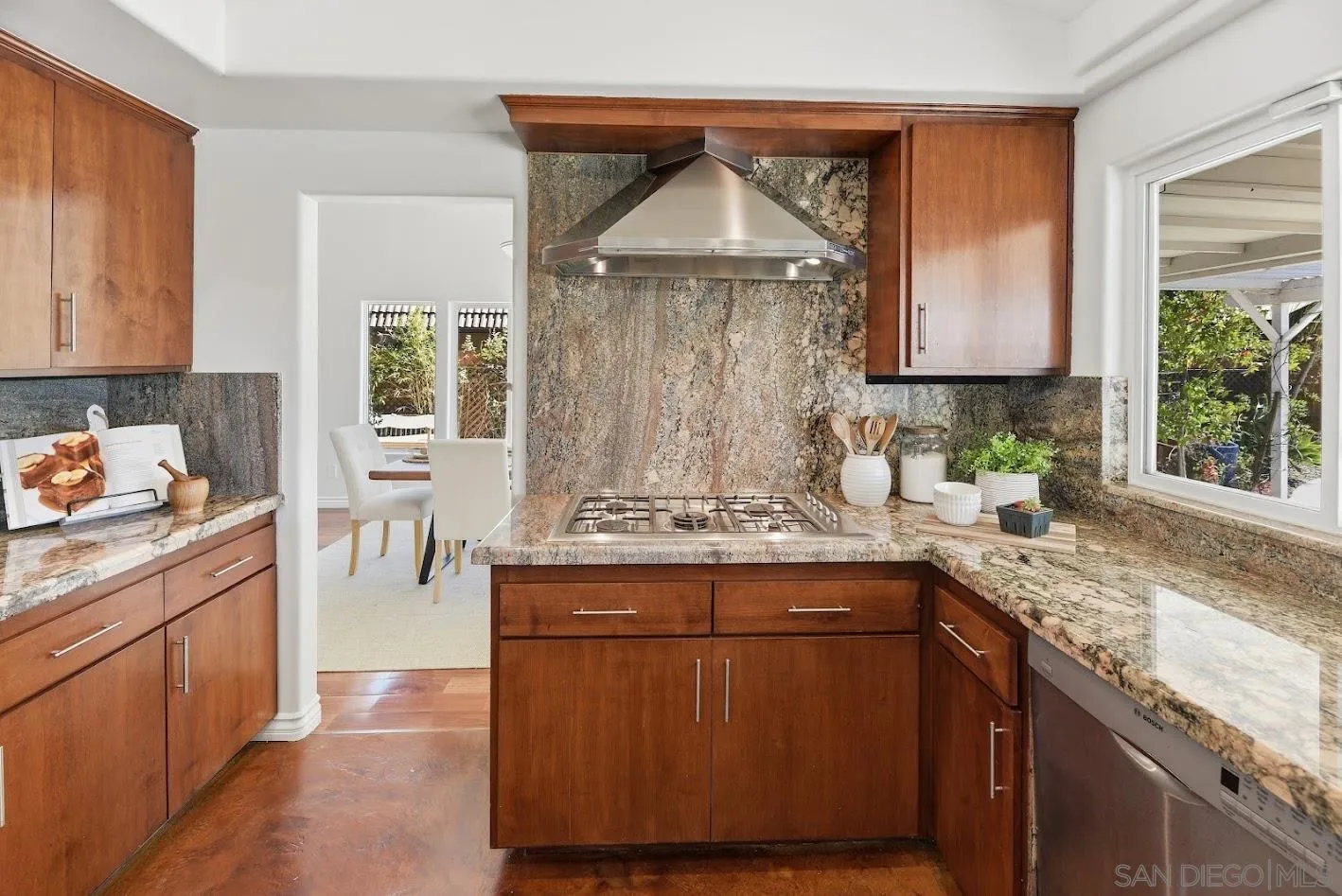 Kitchen with wood cabinets, granite counters and backsplash, and a gas cooktop beneath a stainless steel hood.