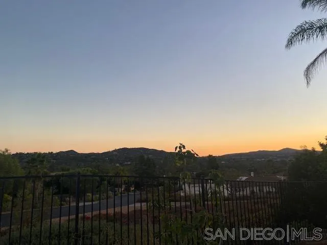 Sunset view over tree-covered hills from behind a black metal railing.