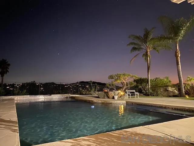 Nighttime swimming pool with palm trees and reflections of patio lights on the water.